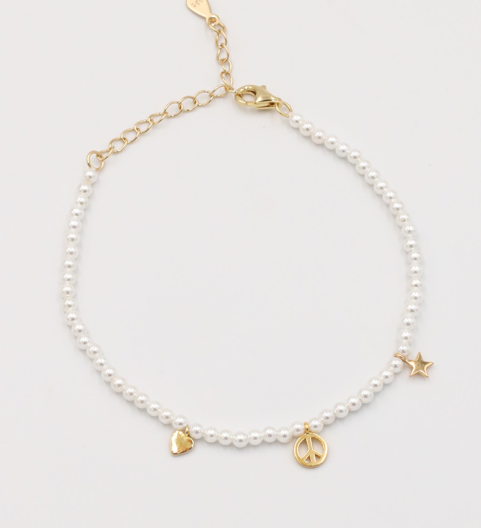 A gold-colored bracelet with white pearl beads and decorative gold beads, featuring a star and a heart charm.