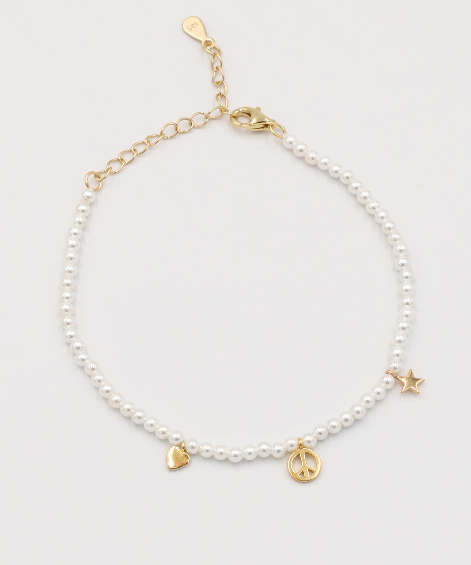 A gold-colored bracelet with white pearl beads and decorative gold beads, featuring a star and a heart charm.