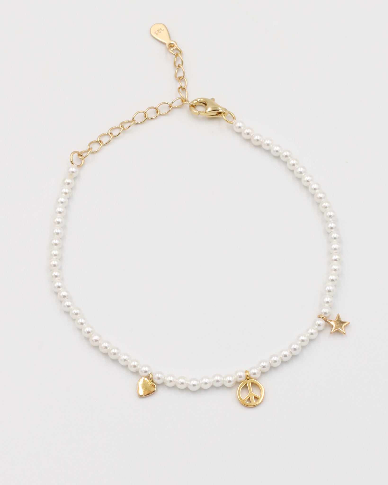A gold-colored bracelet with white pearl beads and decorative gold beads, featuring a star and a heart charm.