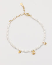A gold-colored bracelet with white pearl beads and decorative gold beads, featuring a star and a heart charm.