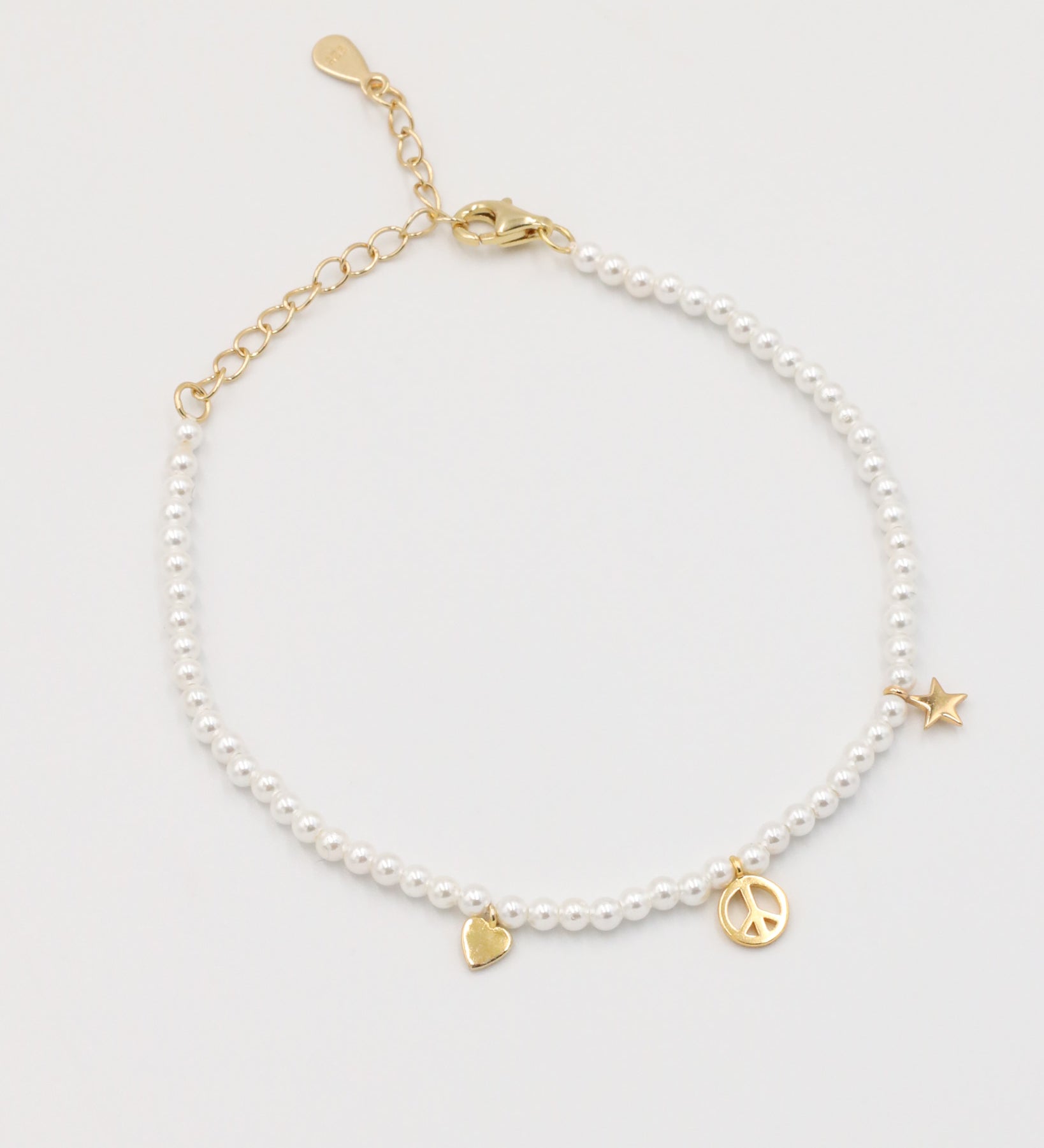 A gold-colored bracelet with white pearl beads and decorative gold beads, featuring a star and a heart charm.