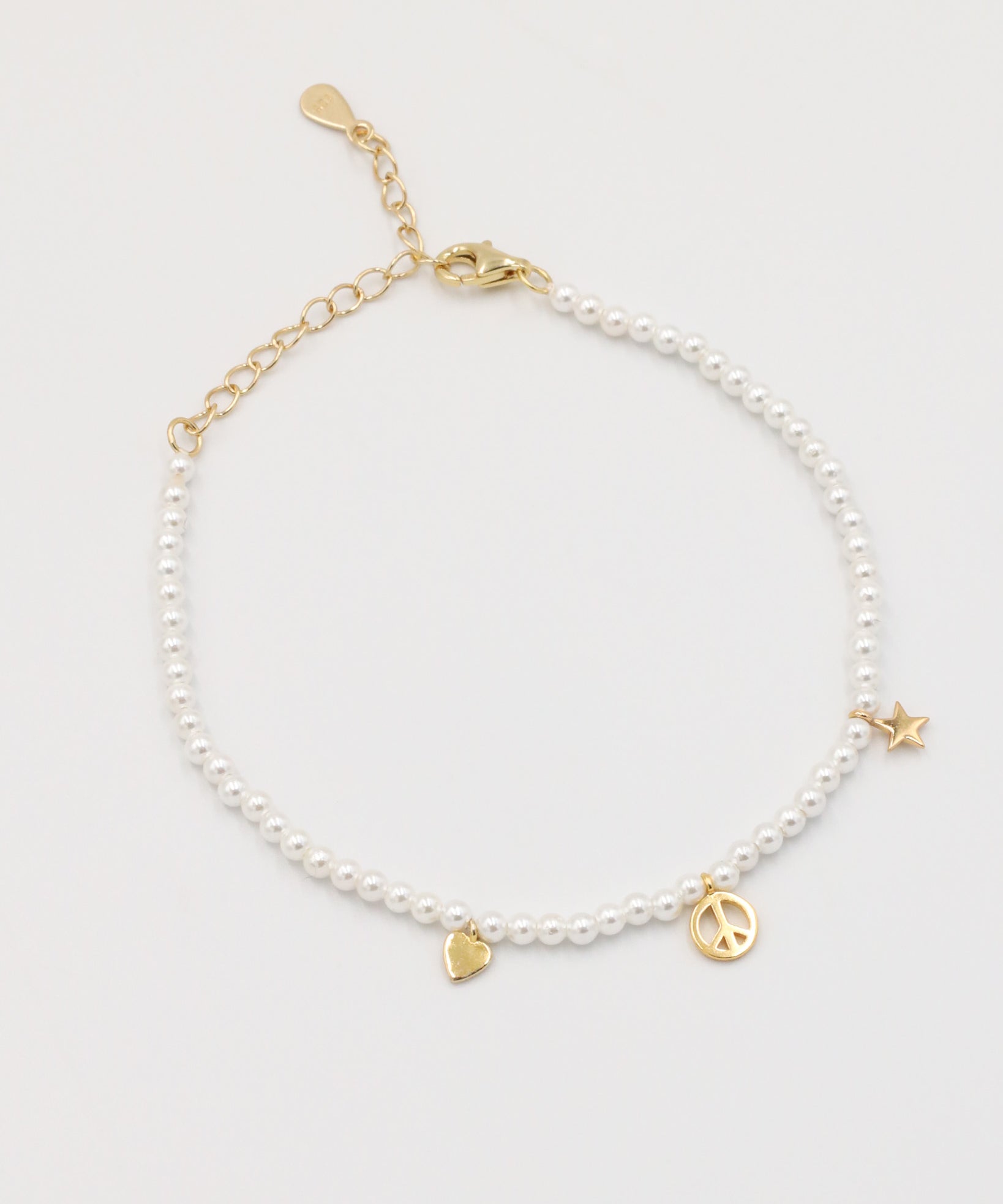 A gold-colored bracelet with white pearl beads and decorative gold beads, featuring a star and a heart charm.