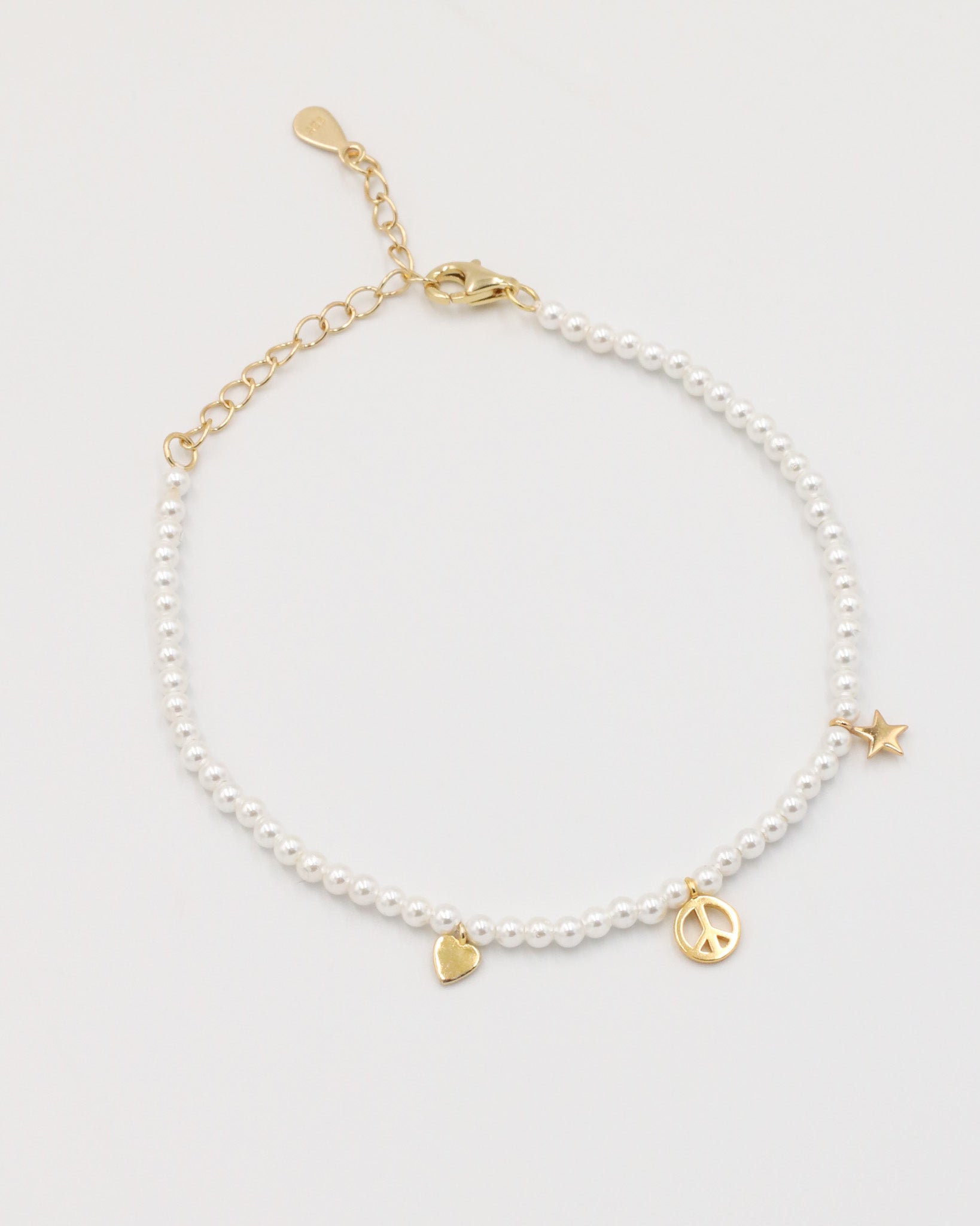 A gold-colored bracelet with white pearl beads and decorative gold beads, featuring a star and a heart charm.