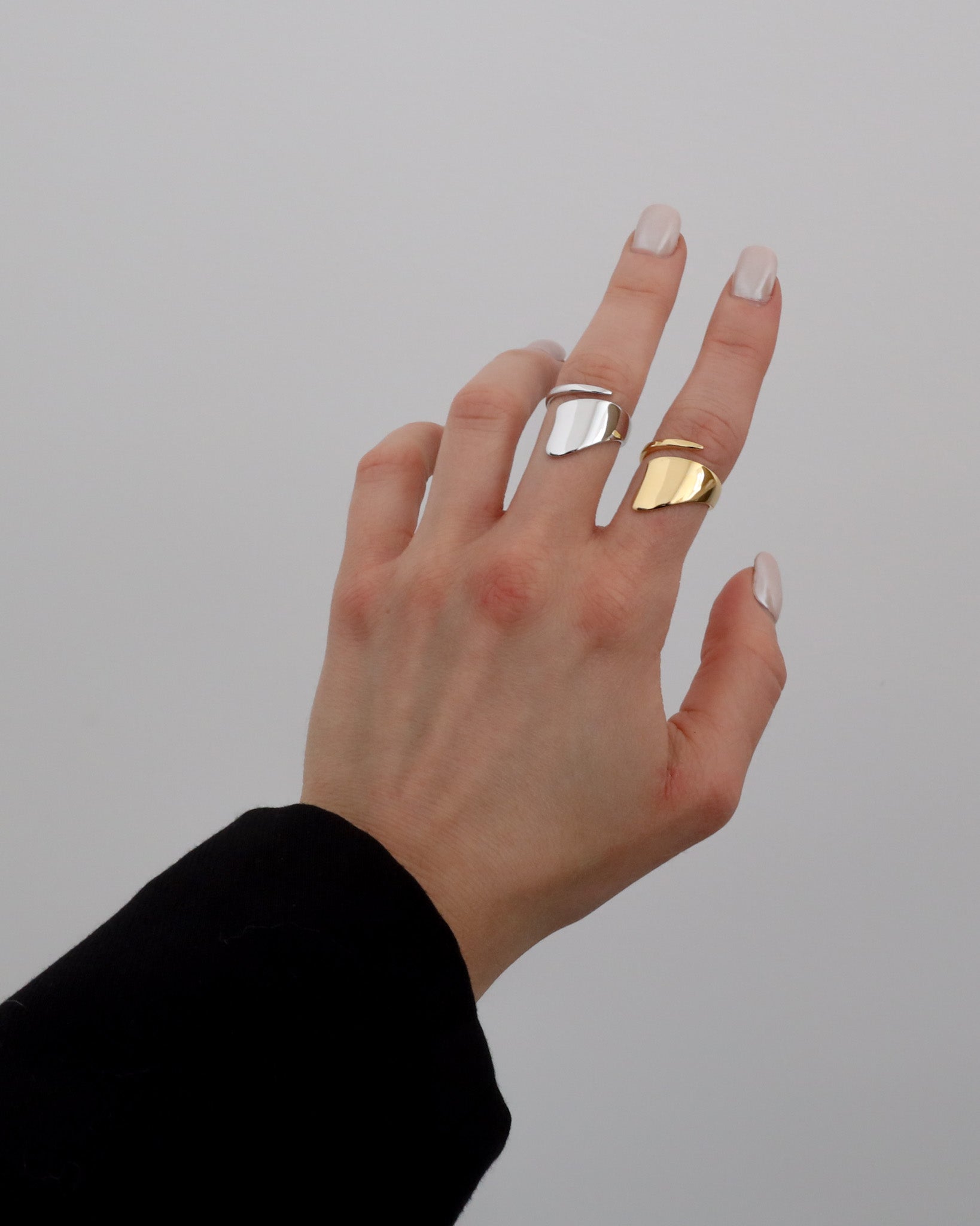 A silver and gold ring with an abstract design worn by a hand.