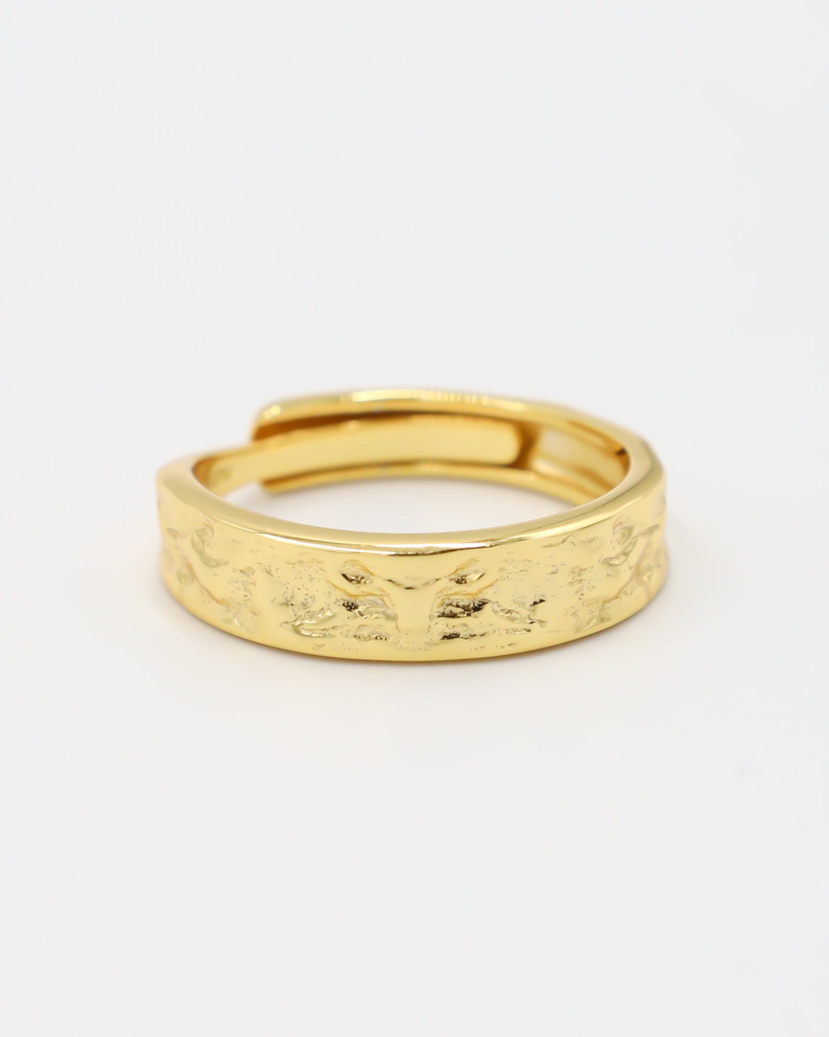 A gold-colored ring with intricate designs lying on a white surface.
