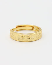 A gold-colored ring with intricate designs lying on a white surface.