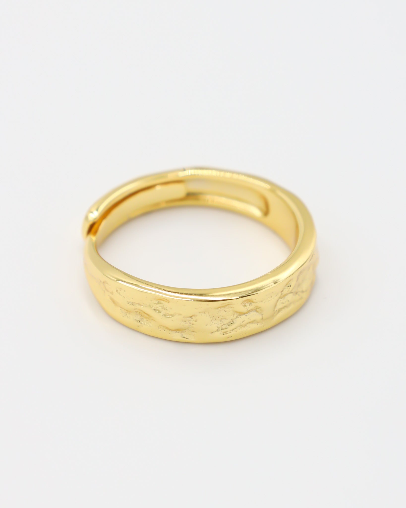 A gold-colored ring with intricate designs lying on a white surface.