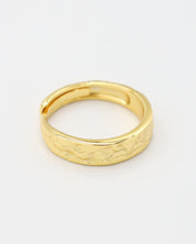 A gold-colored ring with intricate designs lying on a white surface.
