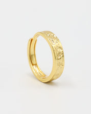 A gold-colored ring with intricate designs on the top surface, displayed against a white background.