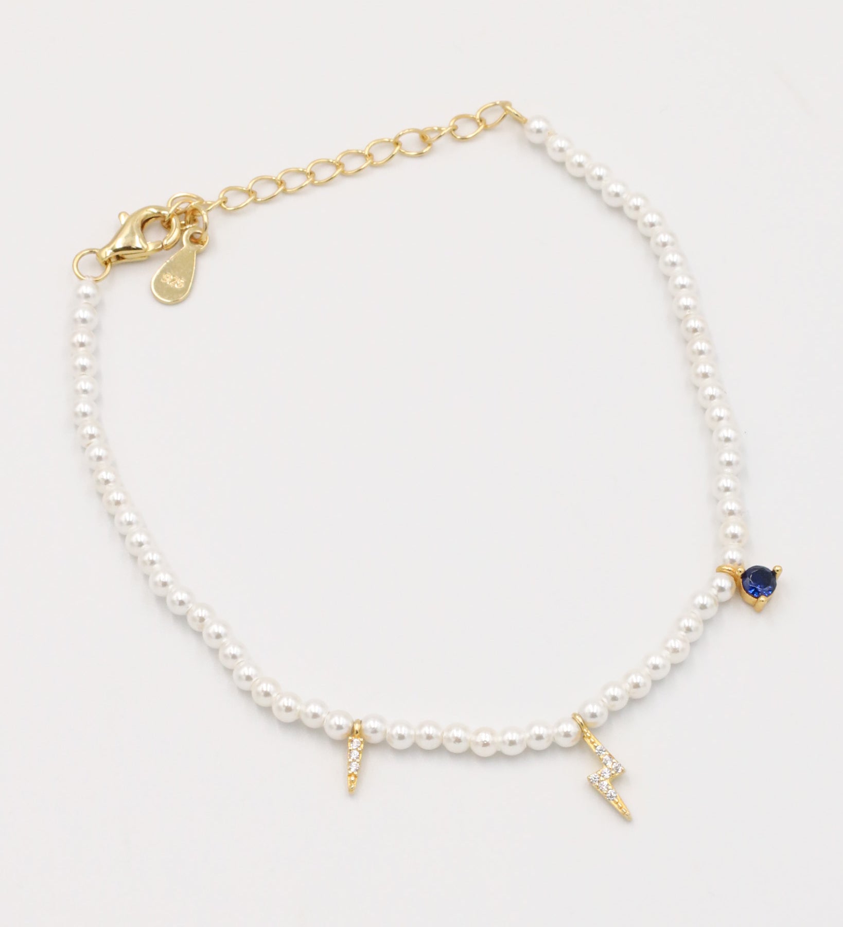 A gold-colored bracelet featuring white pearl beads and small gold charms, including a key-shaped charm.