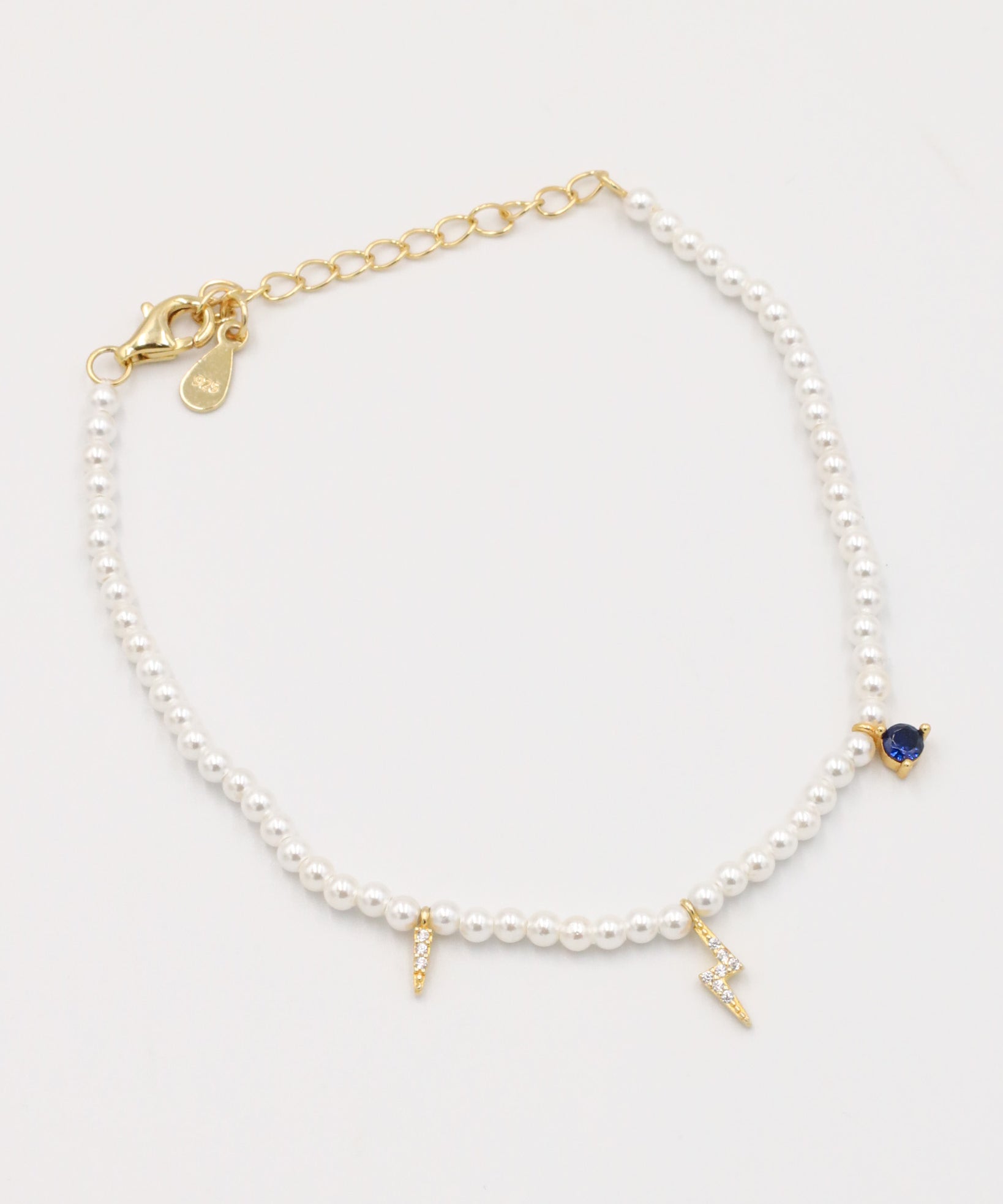 A gold-colored bracelet featuring white pearl beads and small gold charms, including a key-shaped charm.
