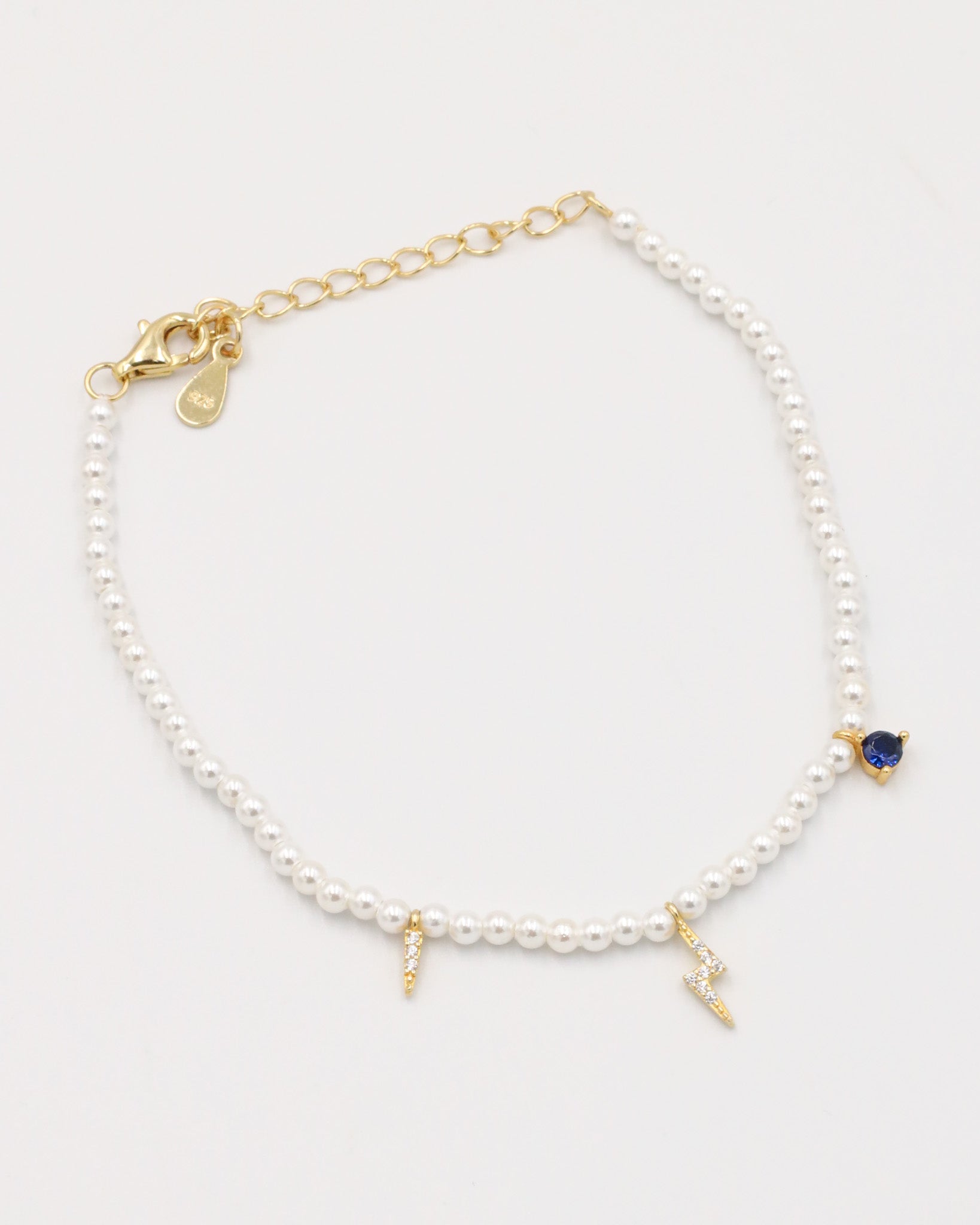 A gold-colored bracelet featuring white pearl beads and small gold charms, including a key-shaped charm.