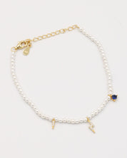 A gold-colored bracelet featuring white pearl beads and small gold charms, including a key-shaped charm.