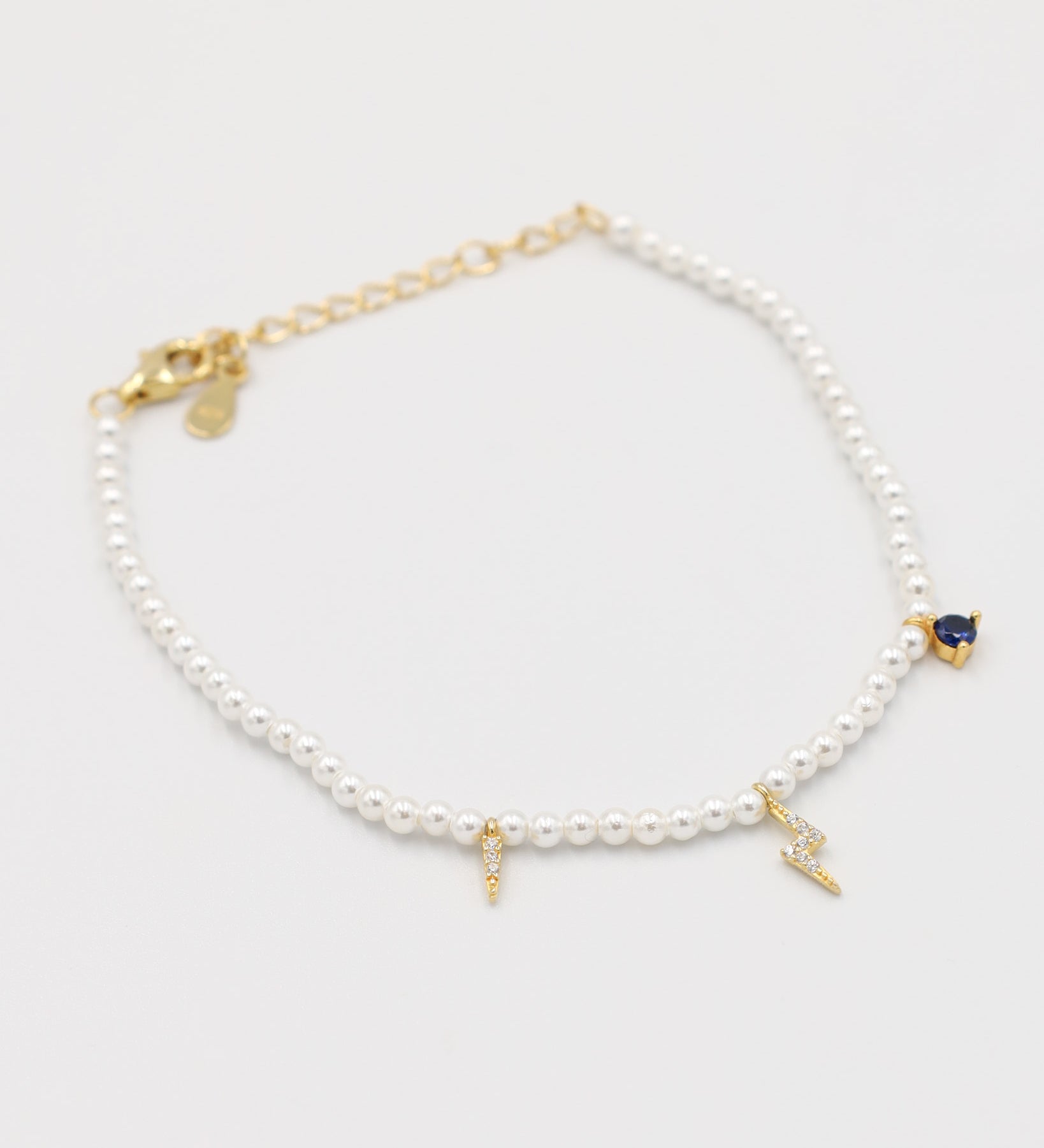 A gold-colored bracelet featuring white pearl beads and small gold charms, including a key-shaped charm.