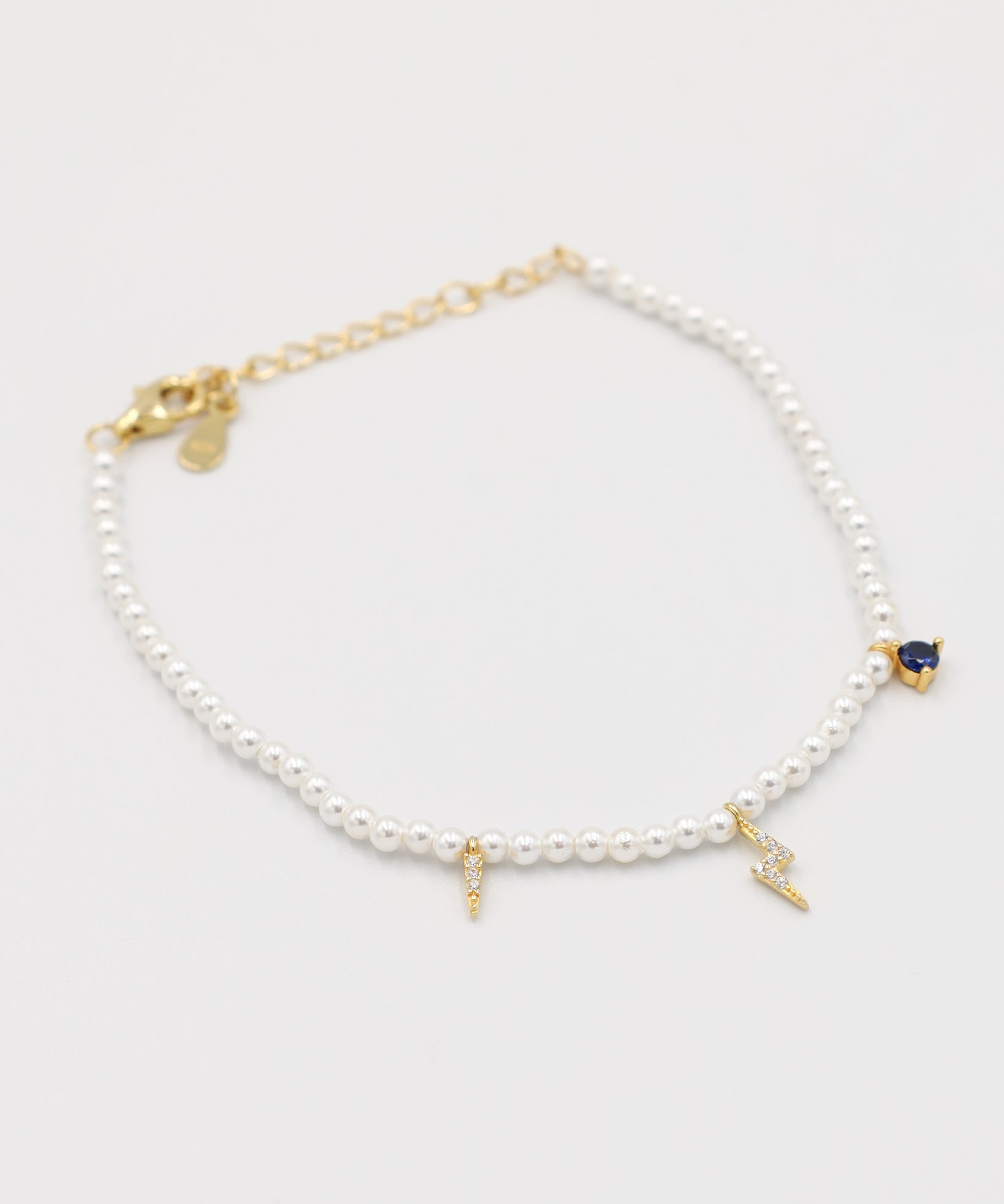 A gold-colored bracelet featuring white pearl beads and small gold charms, including a key-shaped charm.