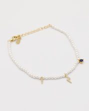 A gold-colored bracelet featuring white pearl beads and small gold charms, including a key-shaped charm.