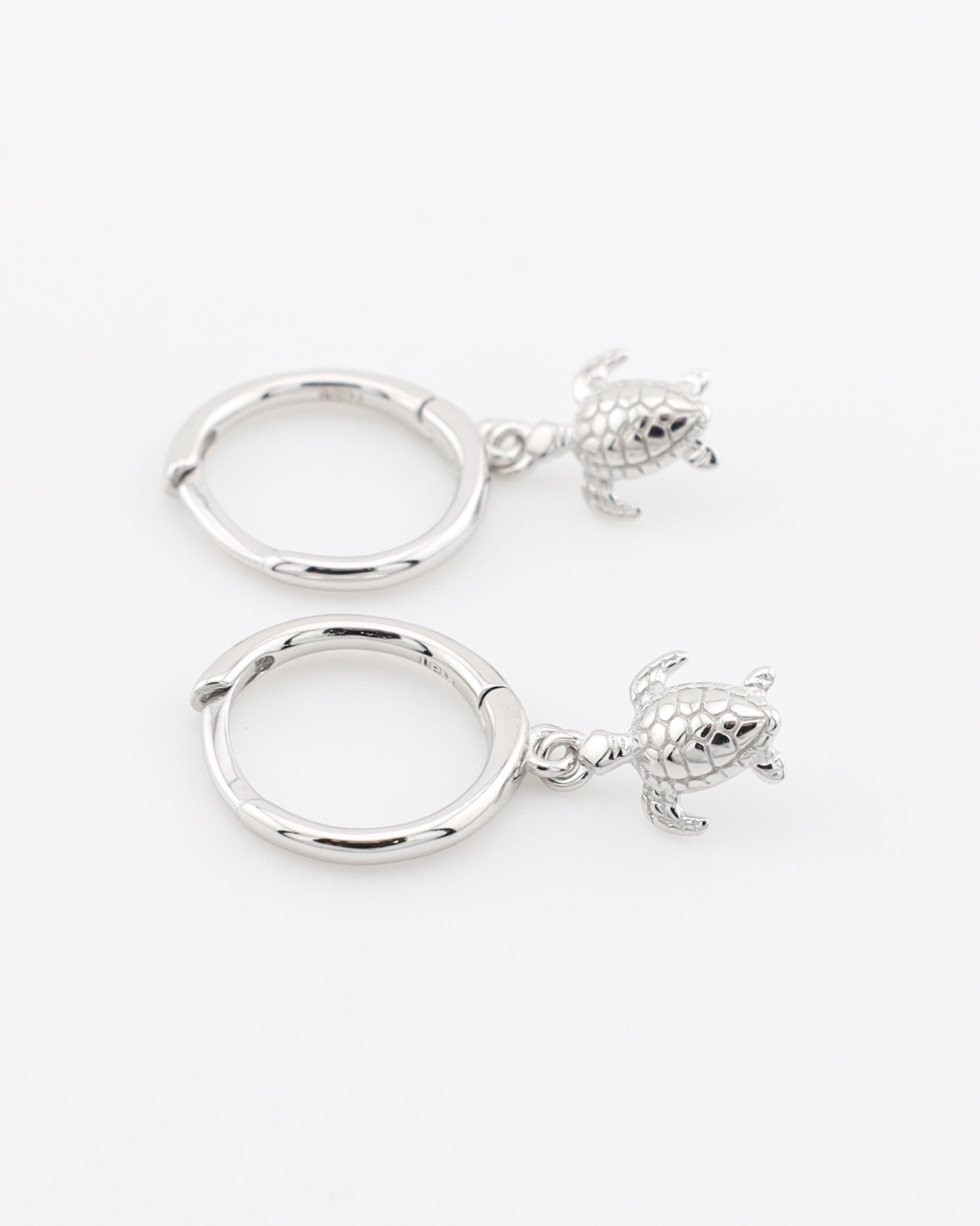 Two silver hoop earrings with turtle charms on a white background