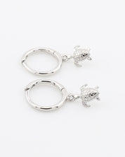 Two silver hoop earrings with turtle charms on a white background