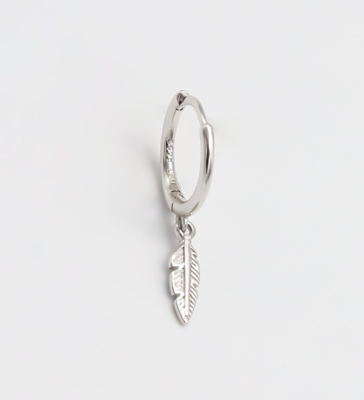 A silver hoop earring with a feather charm attached, displayed against a white background.