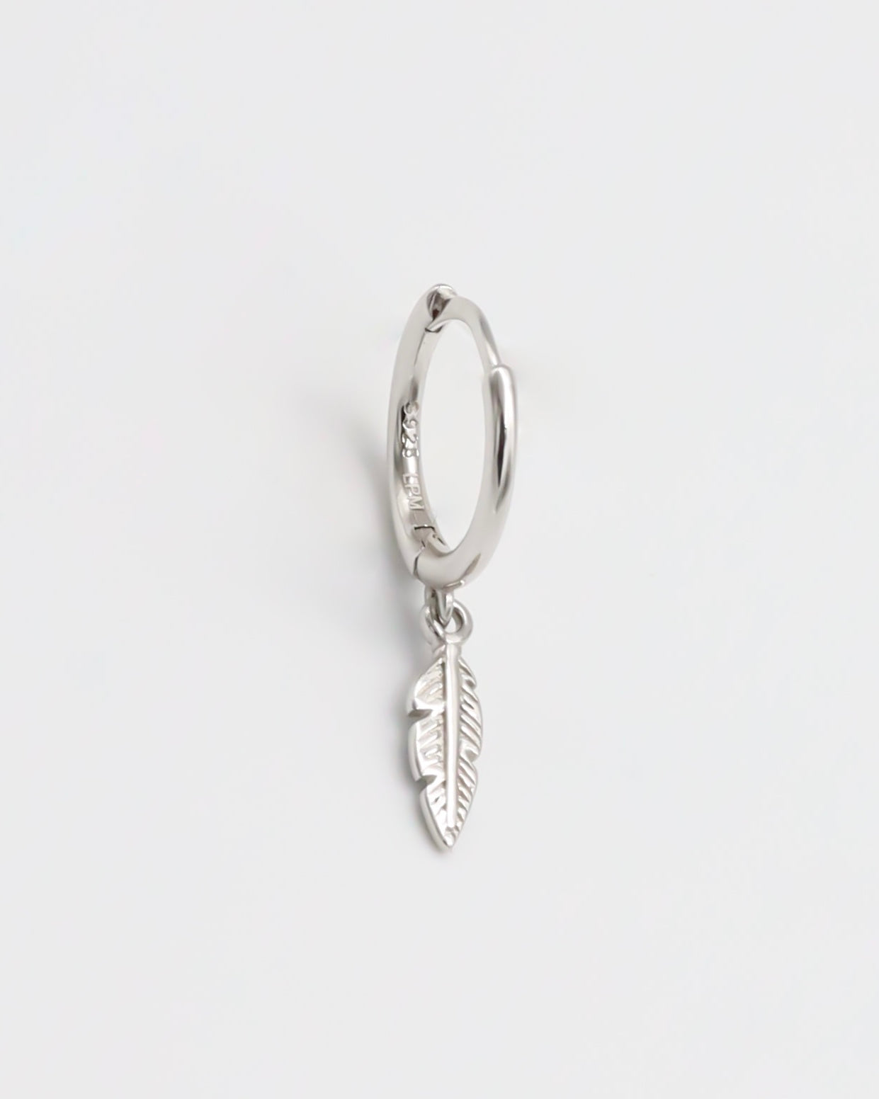 A silver hoop earring with a feather charm attached, displayed against a white background.