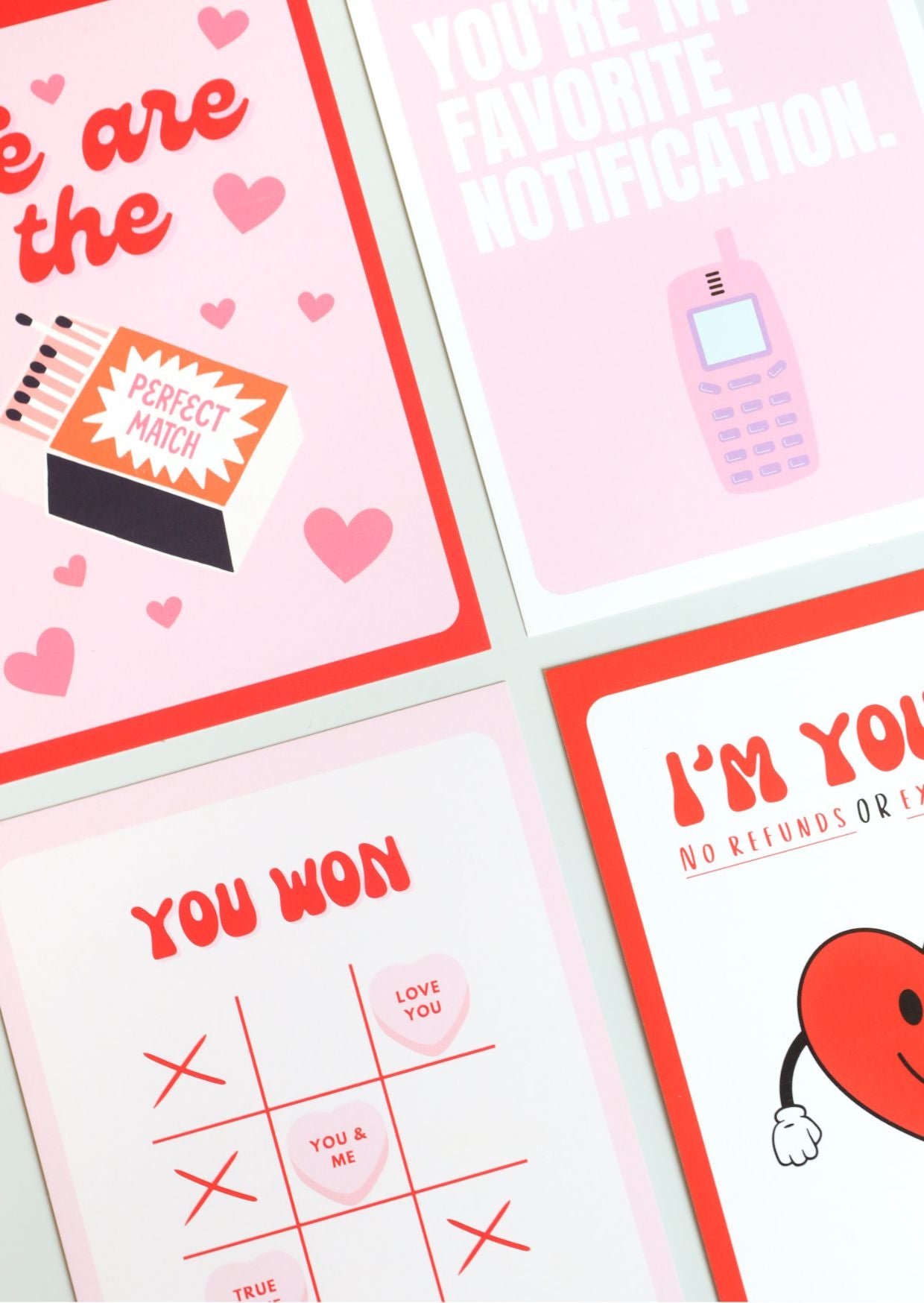 Four playful Valentine’s Day postcards in a bold, pop-art style: one with a matchbox reading “Perfect Match” surrounded by hearts, one saying “You’re my favorite notification” with a retro mobile phone, one with “You won” and a Tic-Tac-Toe layout using candy hearts, and one featuring a smiling heart with the phrase “I’m yours – no refunds.” 
