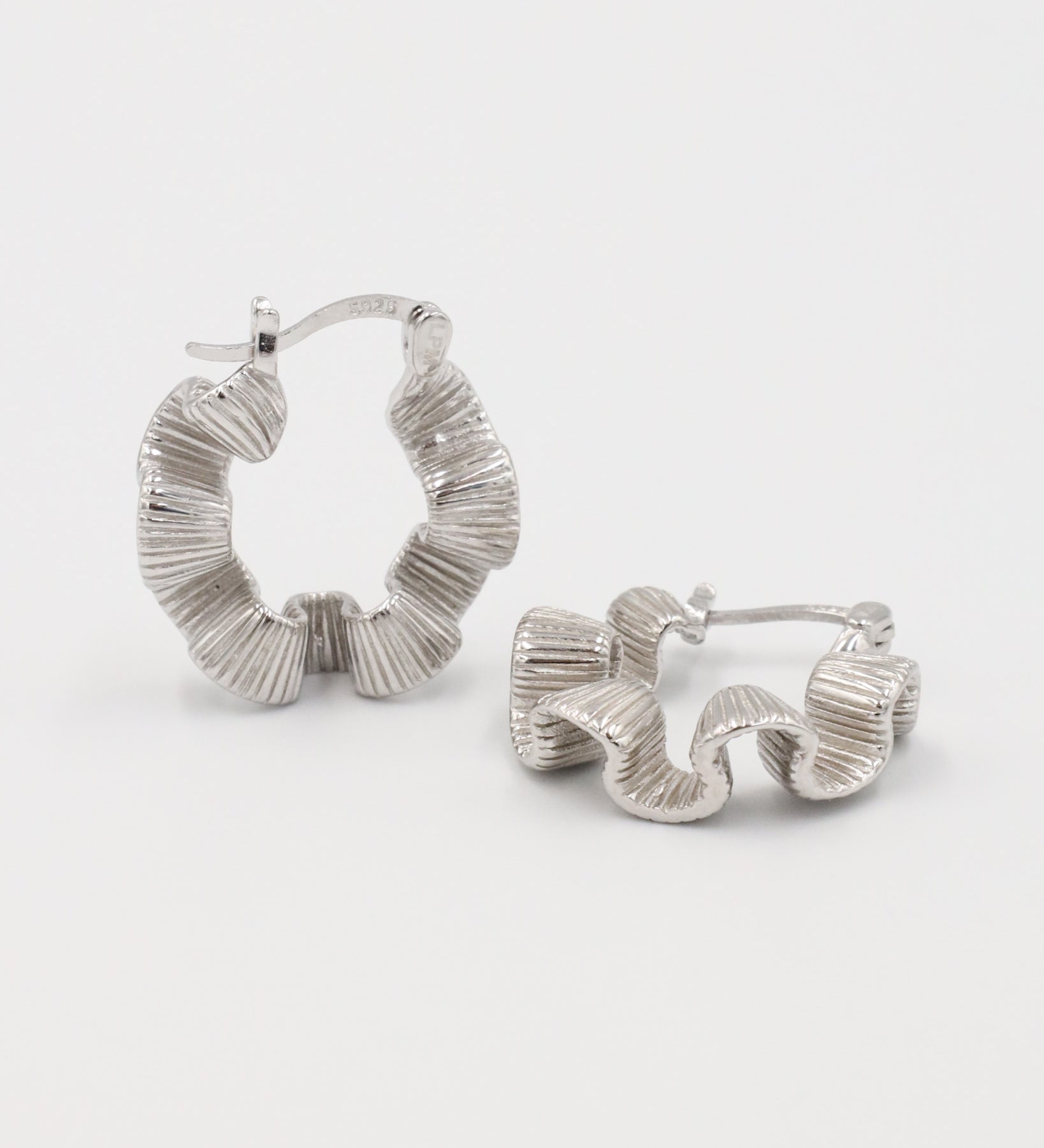 A pair of silver creole earrings with a latch back clasp, displayed against a white background.