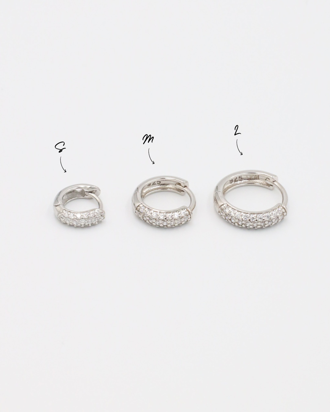 Three sizes of Billie hoop earrings in silver with zirconia stones, displayed from a side view. Sizes shown: S, M, and L.