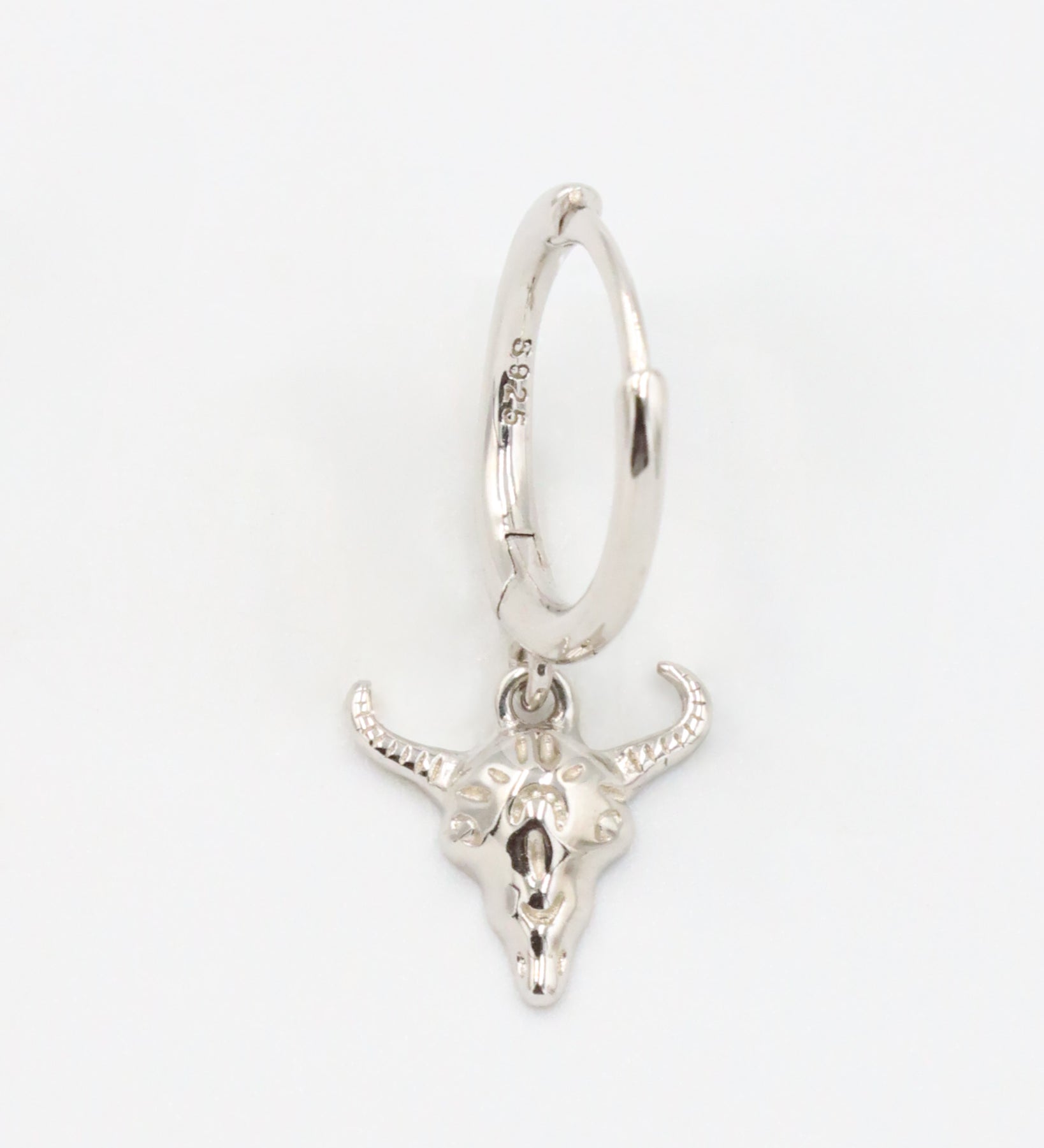 Close-up of a sterling silver hoop earring featuring a detailed bull skull charm, front view.