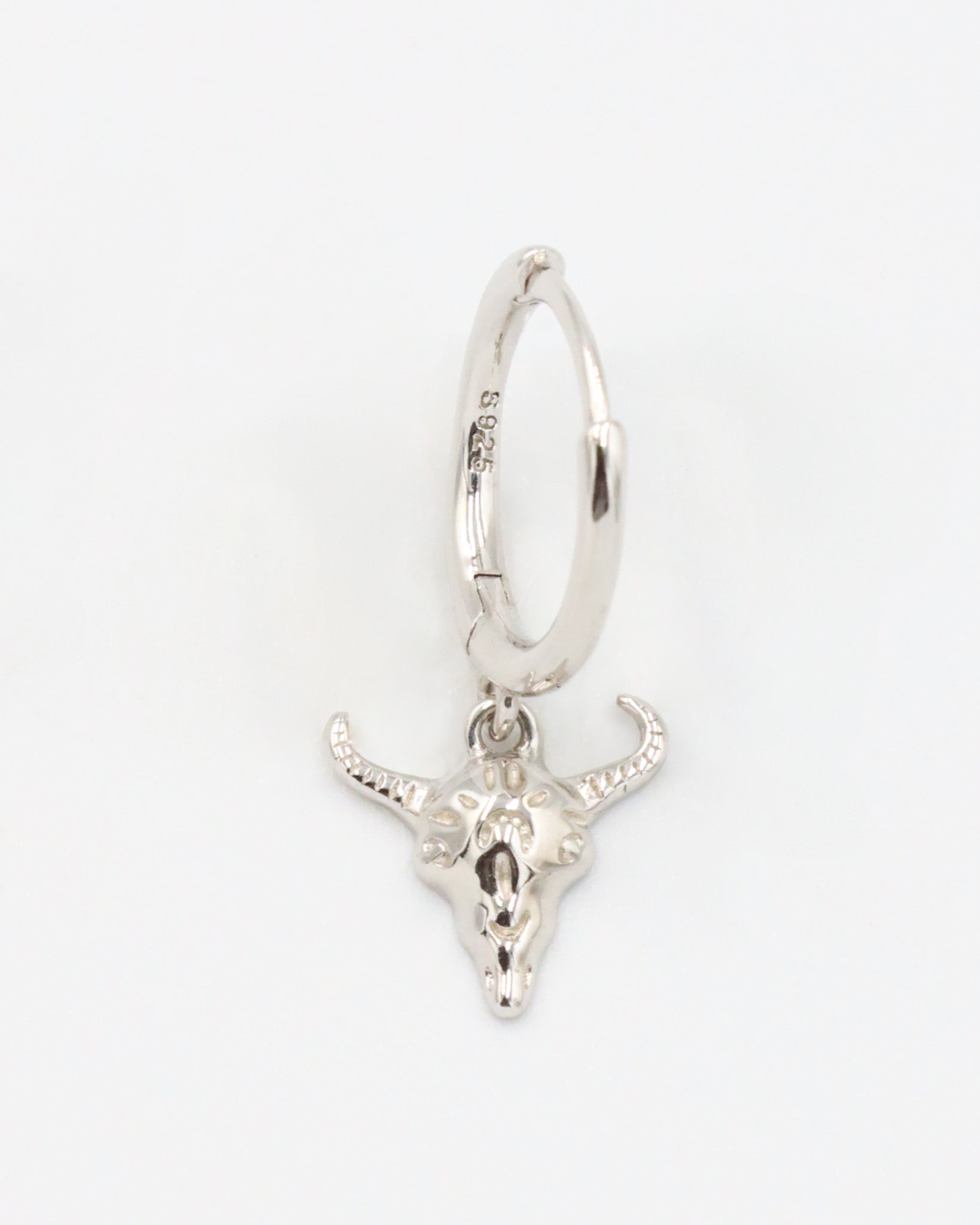 Close-up of a sterling silver hoop earring featuring a detailed bull skull charm, front view.