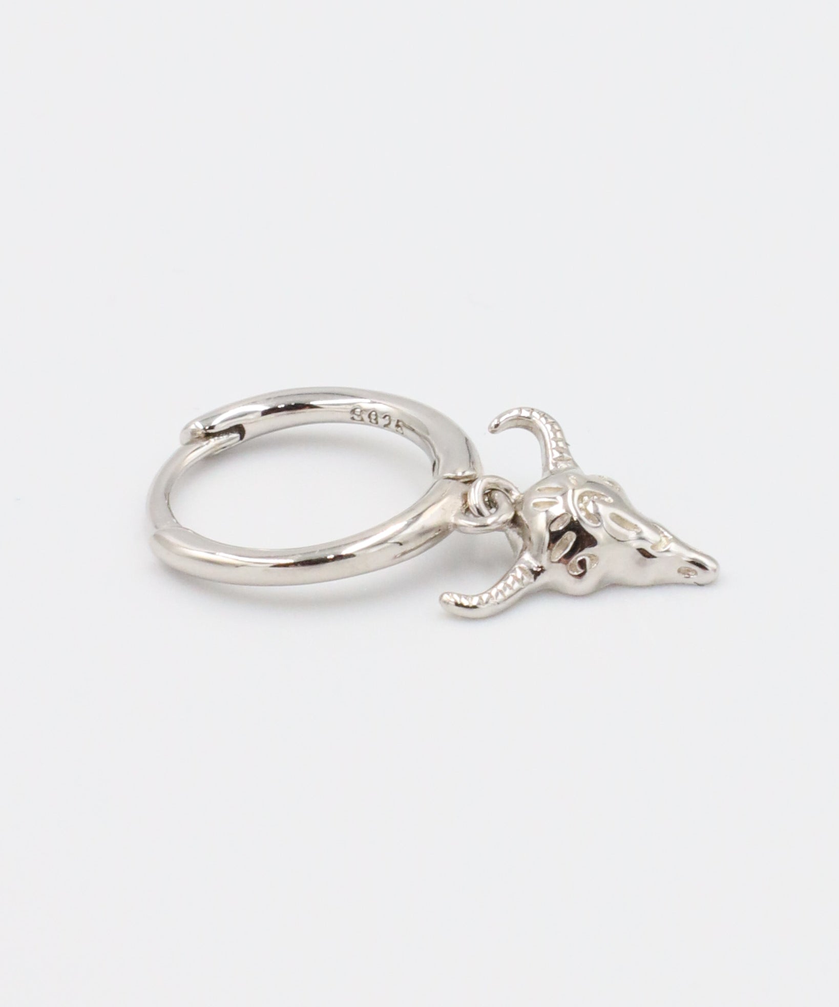 Single sterling silver hoop earring with a hanging bull skull charm, displayed at a side angle.