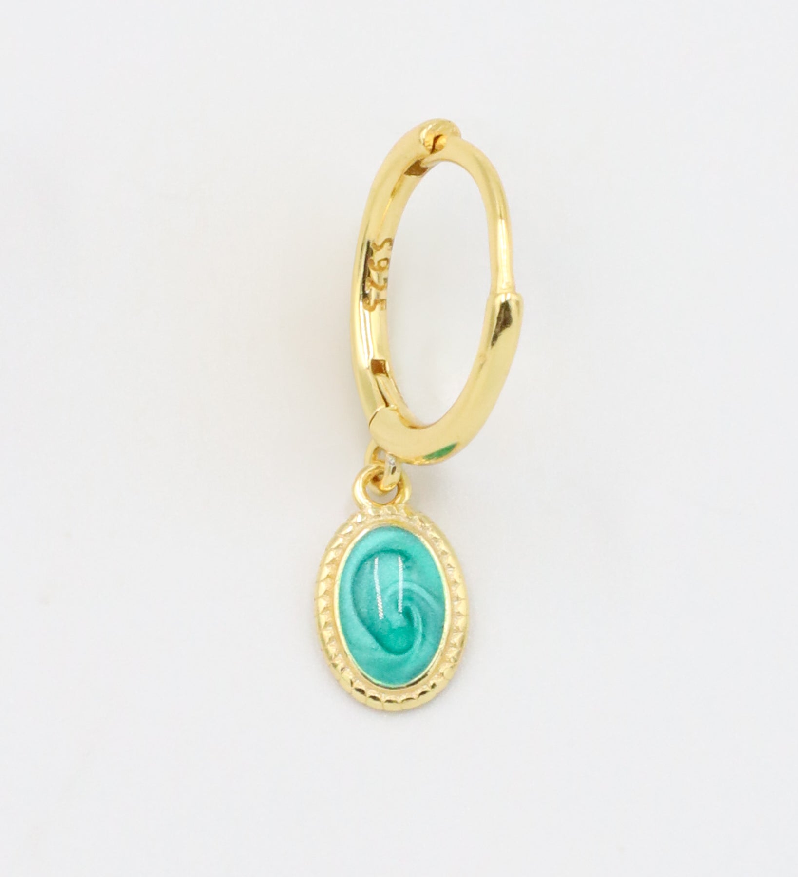 A close-up of a single gold-plated sterling silver hoop earring with an oval turquoise charm, displayed from the front.
