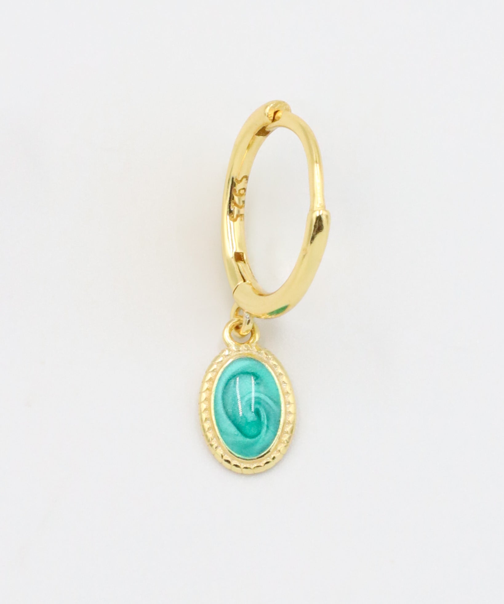 A close-up of a single gold-plated sterling silver hoop earring with an oval turquoise charm, displayed from the front.
