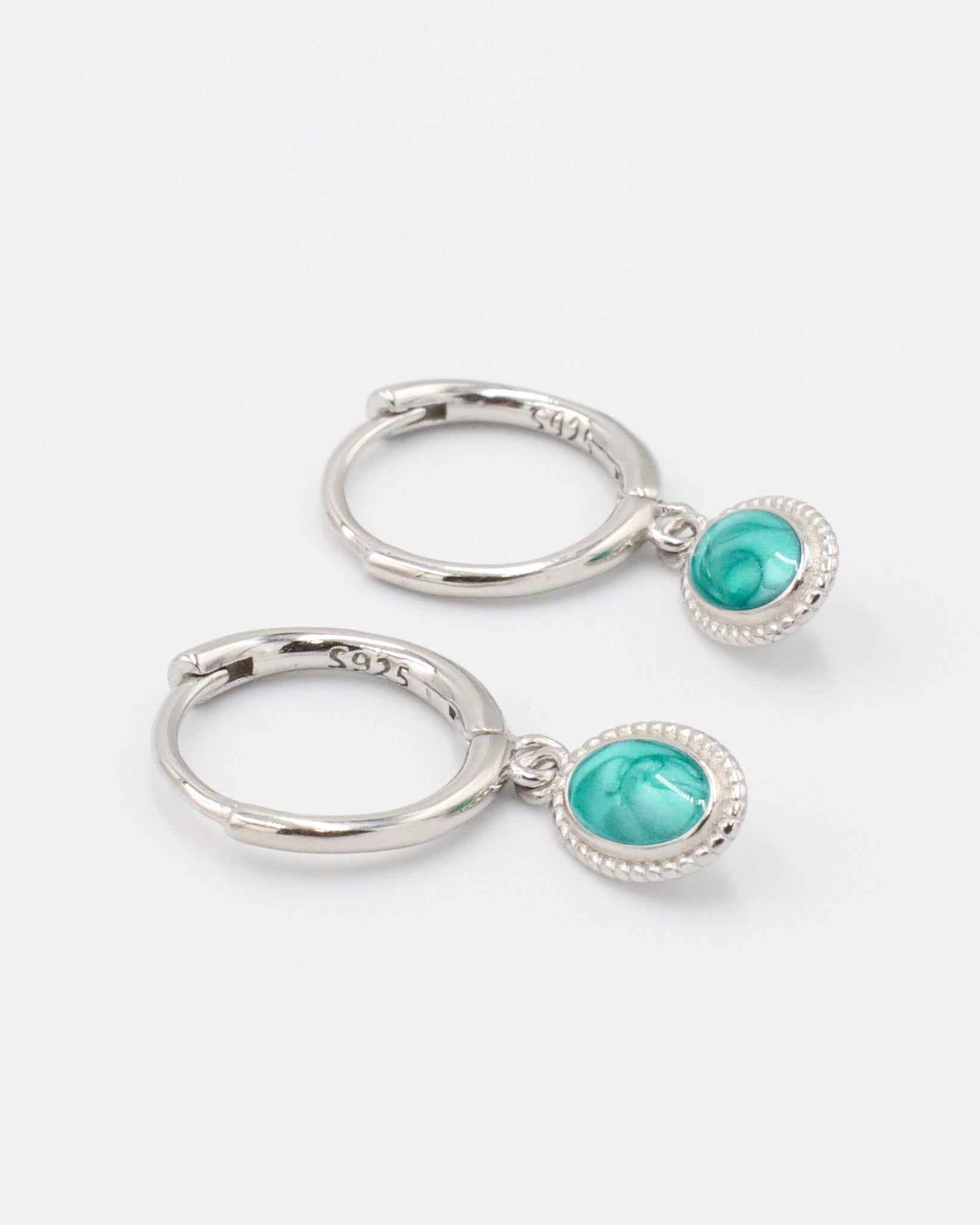 Pair of Josefine Silver hoop earrings with a turquoise oval pendant on sterling silver hoops.
