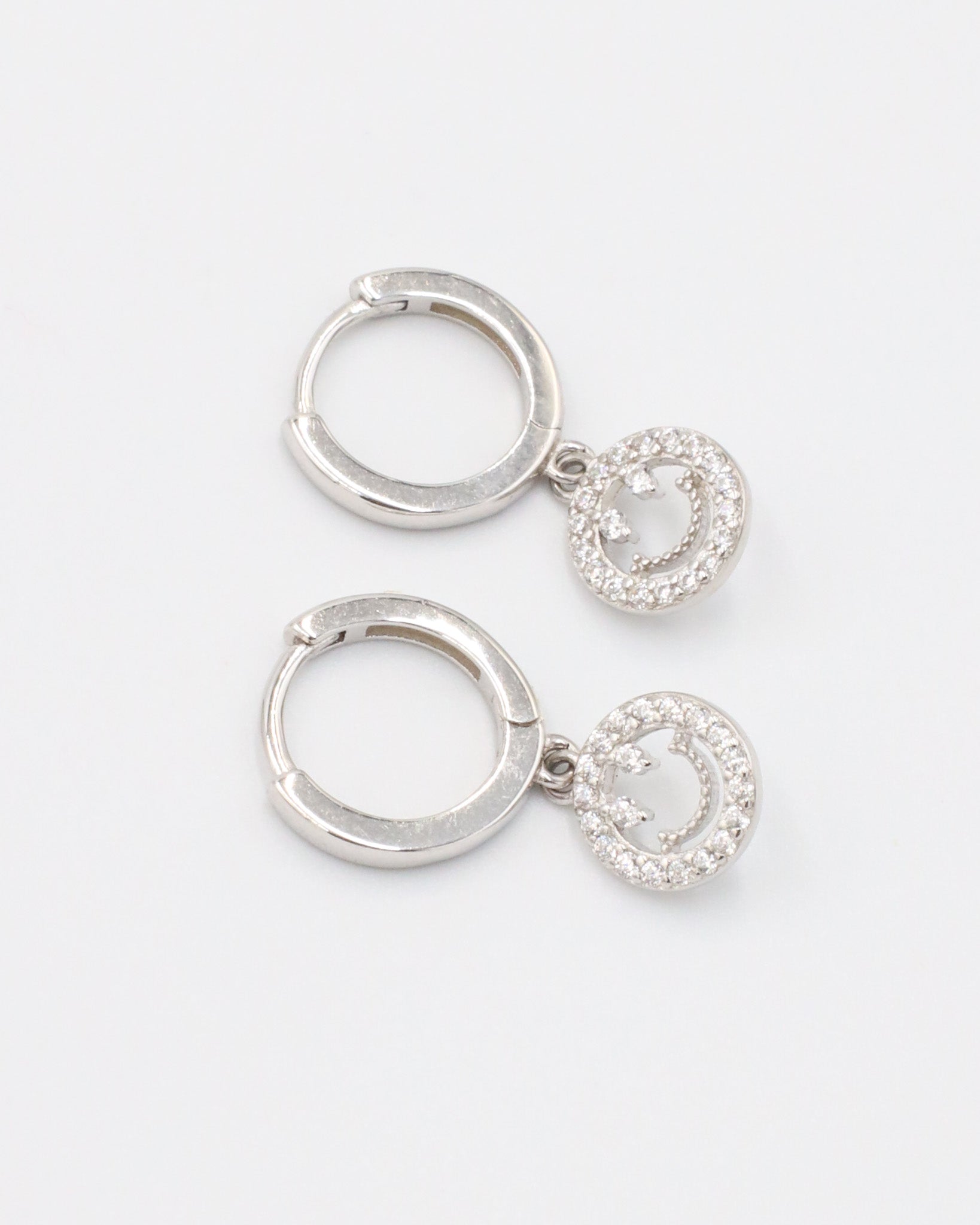 A pair of sterling silver hoop earrings with smiley face pendants paved with zirconia stones.