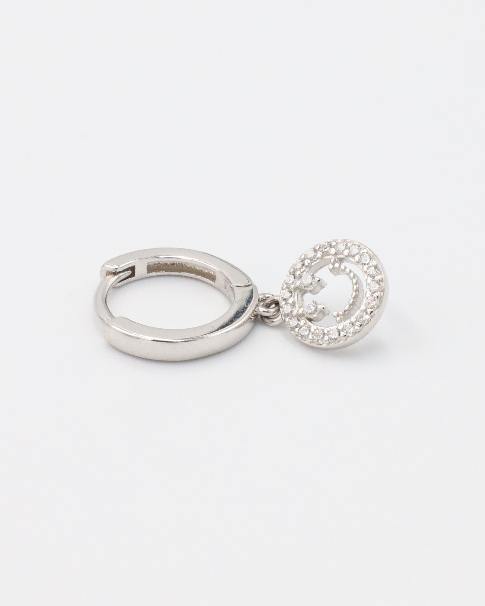 A single sterling silver hoop earring with a smiley face pendant paved with zirconia stones.