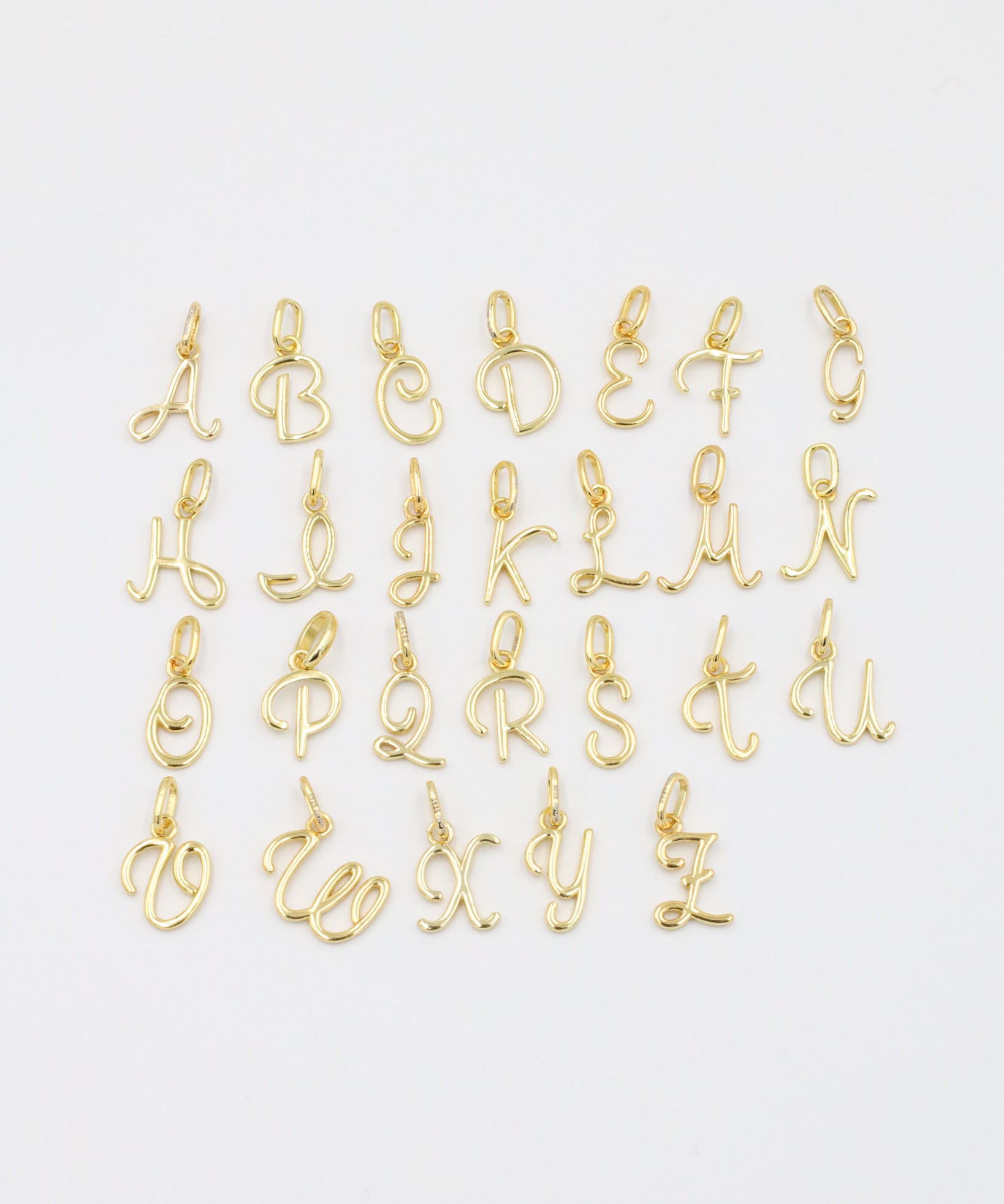 A set of gold-plated letter curve alphabet pendants spread flat in a display.