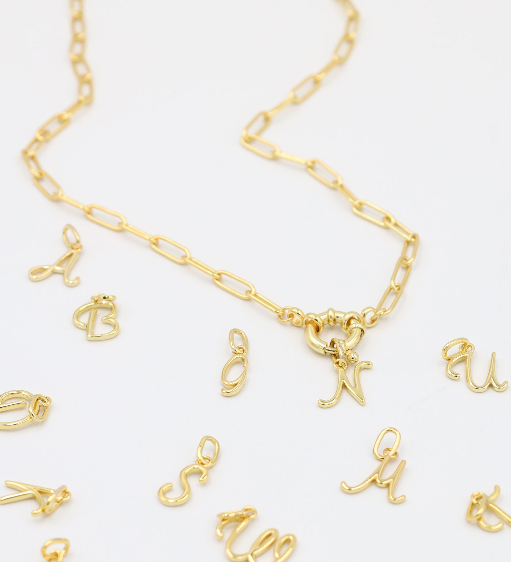 Gold-plated letter curve pendants displayed with a matching gold chain necklace.