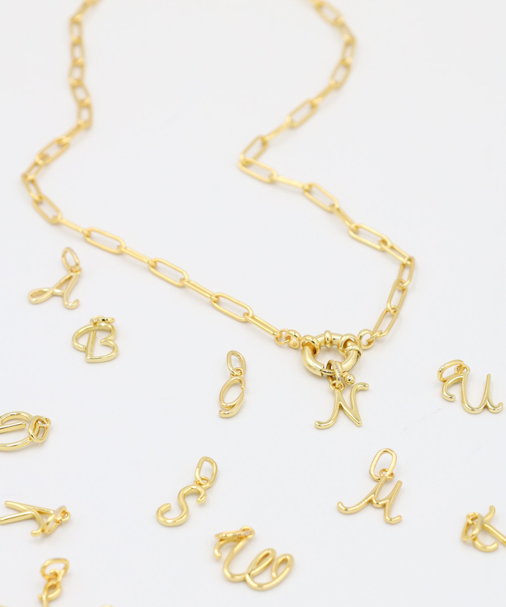 Gold-plated letter curve pendants displayed with a matching gold chain necklace.