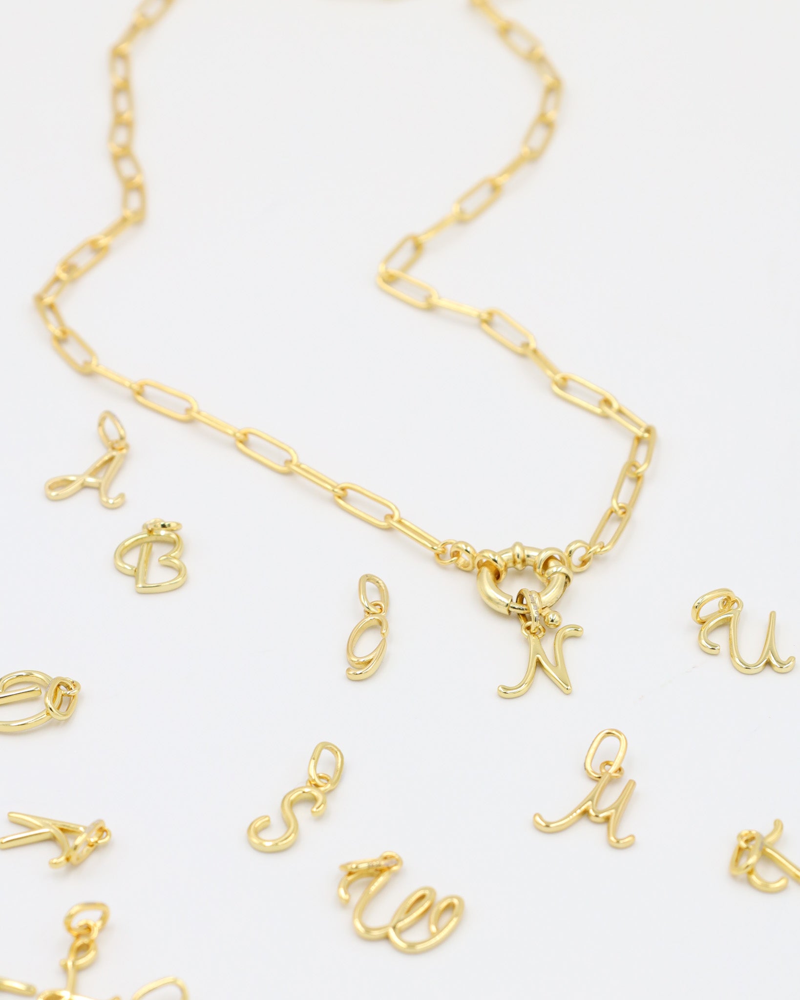 Gold-plated letter curve pendants displayed with a matching gold chain necklace.