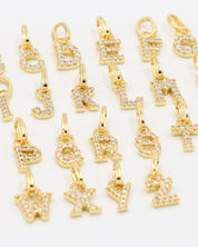 Close-up view of gold-plated letter pendants with zirconia stones, displaying intricate detailing of each letter charm.