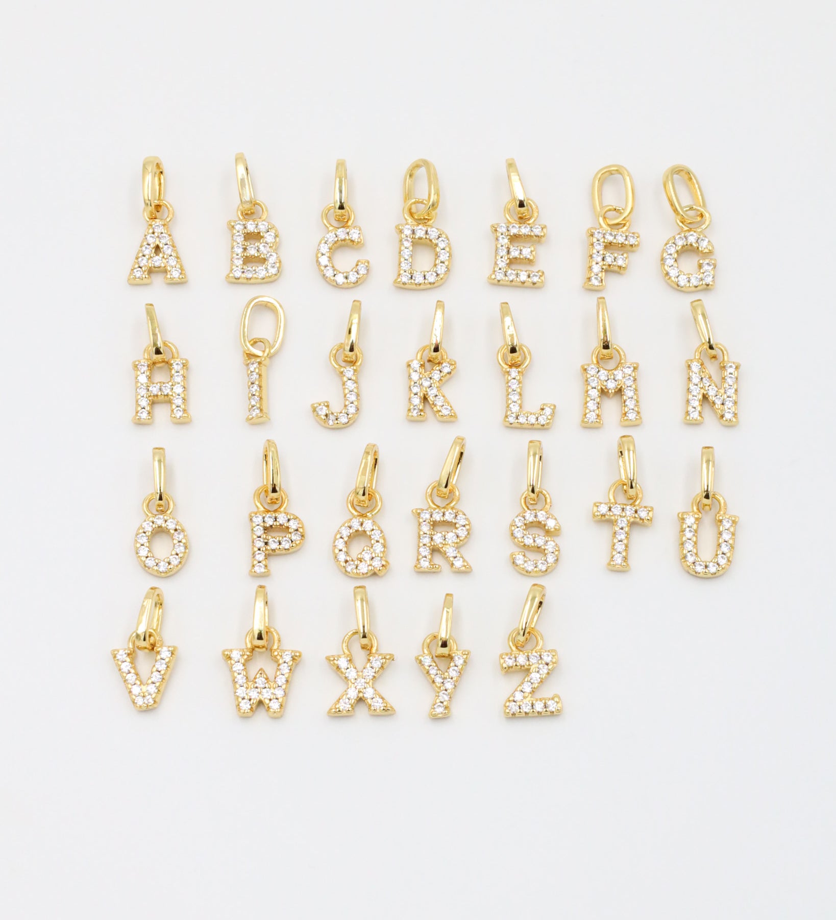 Gold-plated sparkly letter pendants arranged in a complete A-Z display, showcasing their zirconia embellishments.