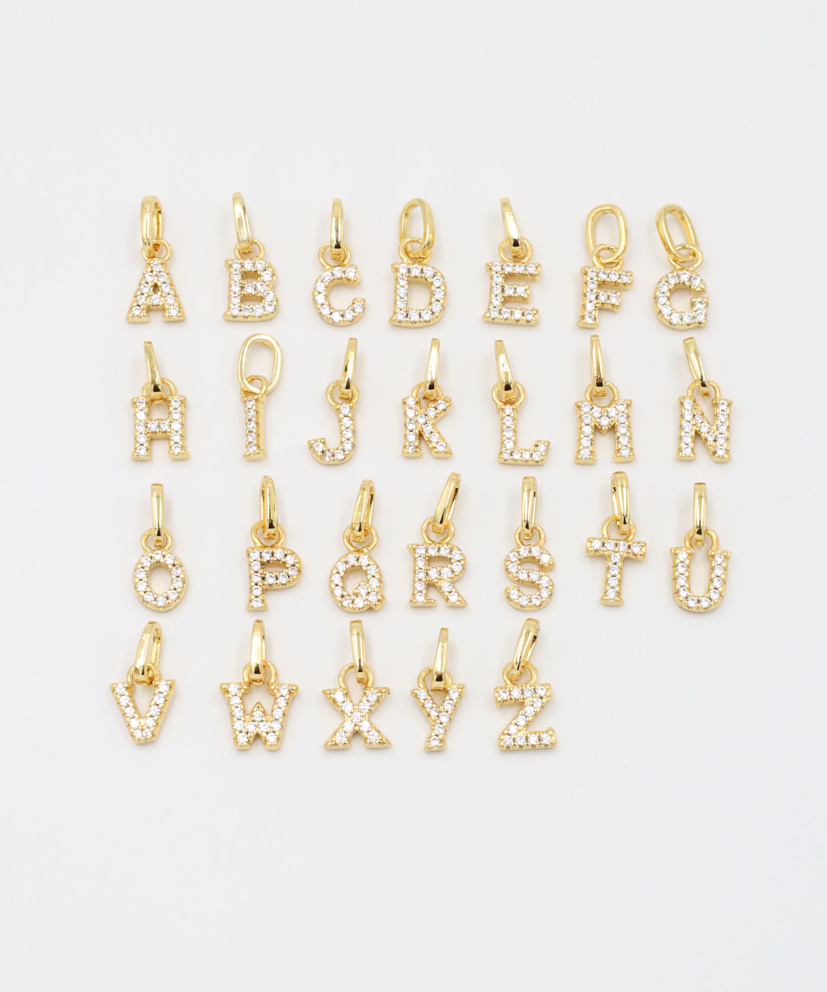 Gold-plated sparkly letter pendants arranged in a complete A-Z display, showcasing their zirconia embellishments.