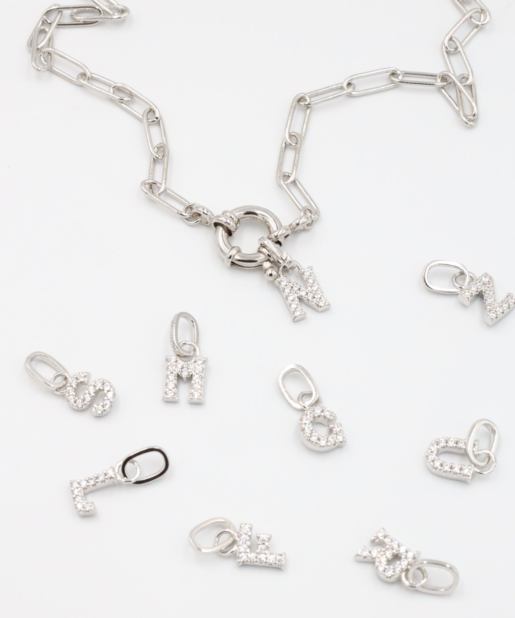 Sterling silver alphabet pendants adorned with zirconia stones, displayed with a chain.