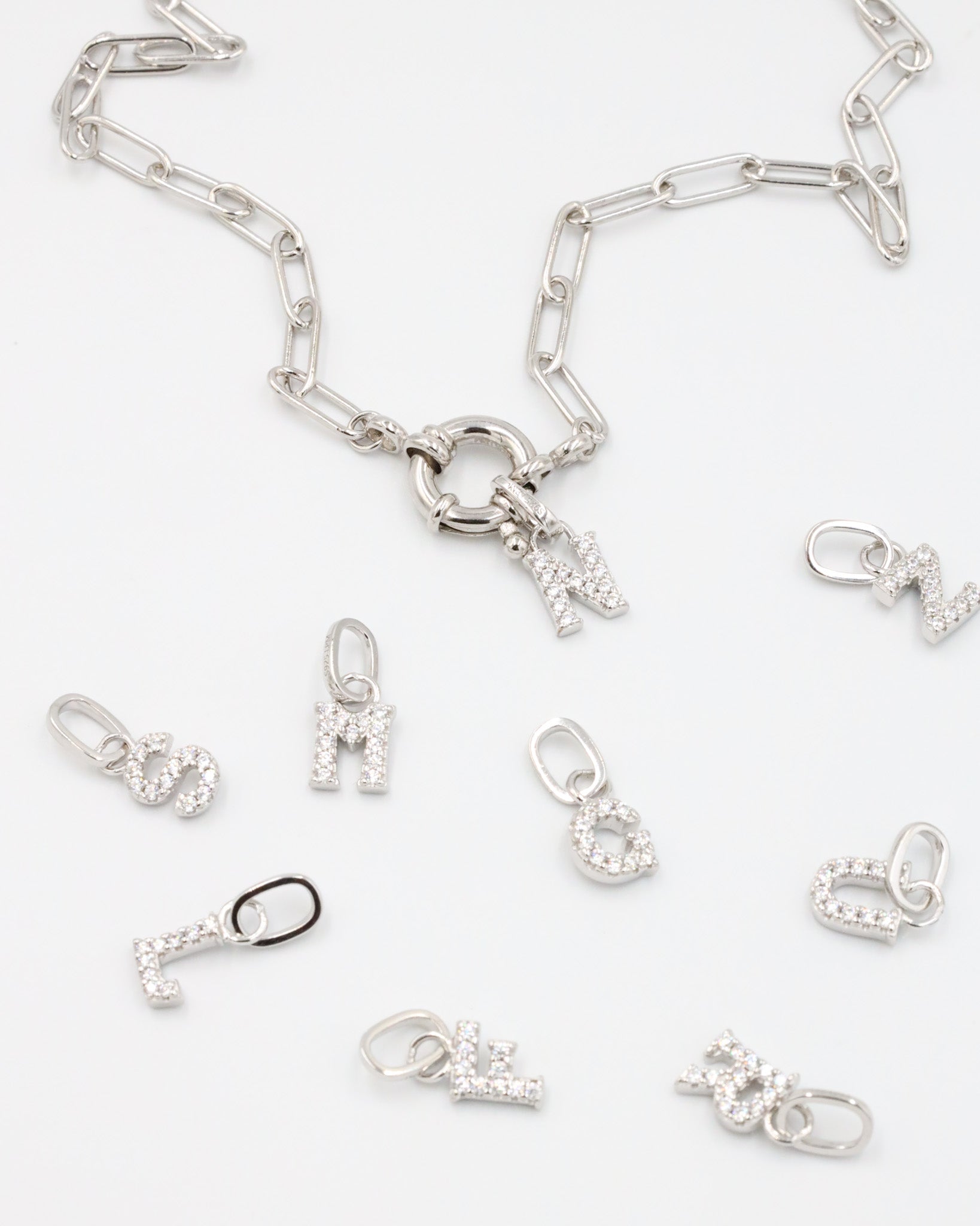 Sterling silver alphabet pendants adorned with zirconia stones, displayed with a chain.