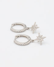 A pair of "Nova Silver" huggie earrings made from sterling silver, featuring cubic zirconia stones arranged in a star-shaped pendant with pave detailing on the hoops.