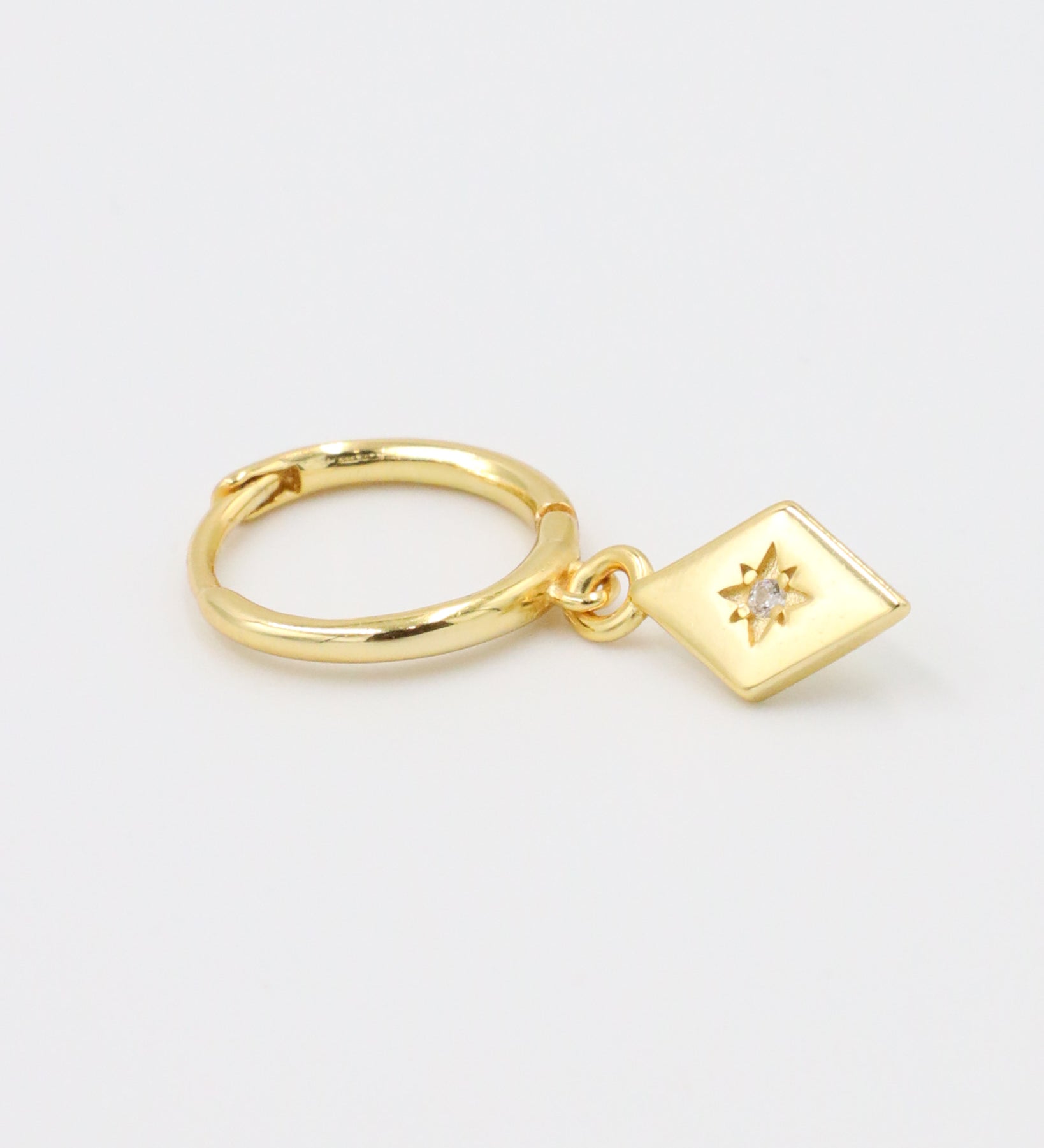 Single Patricia Gold earring featuring a starburst design with a zirconia center, hanging from a gold hoop.
