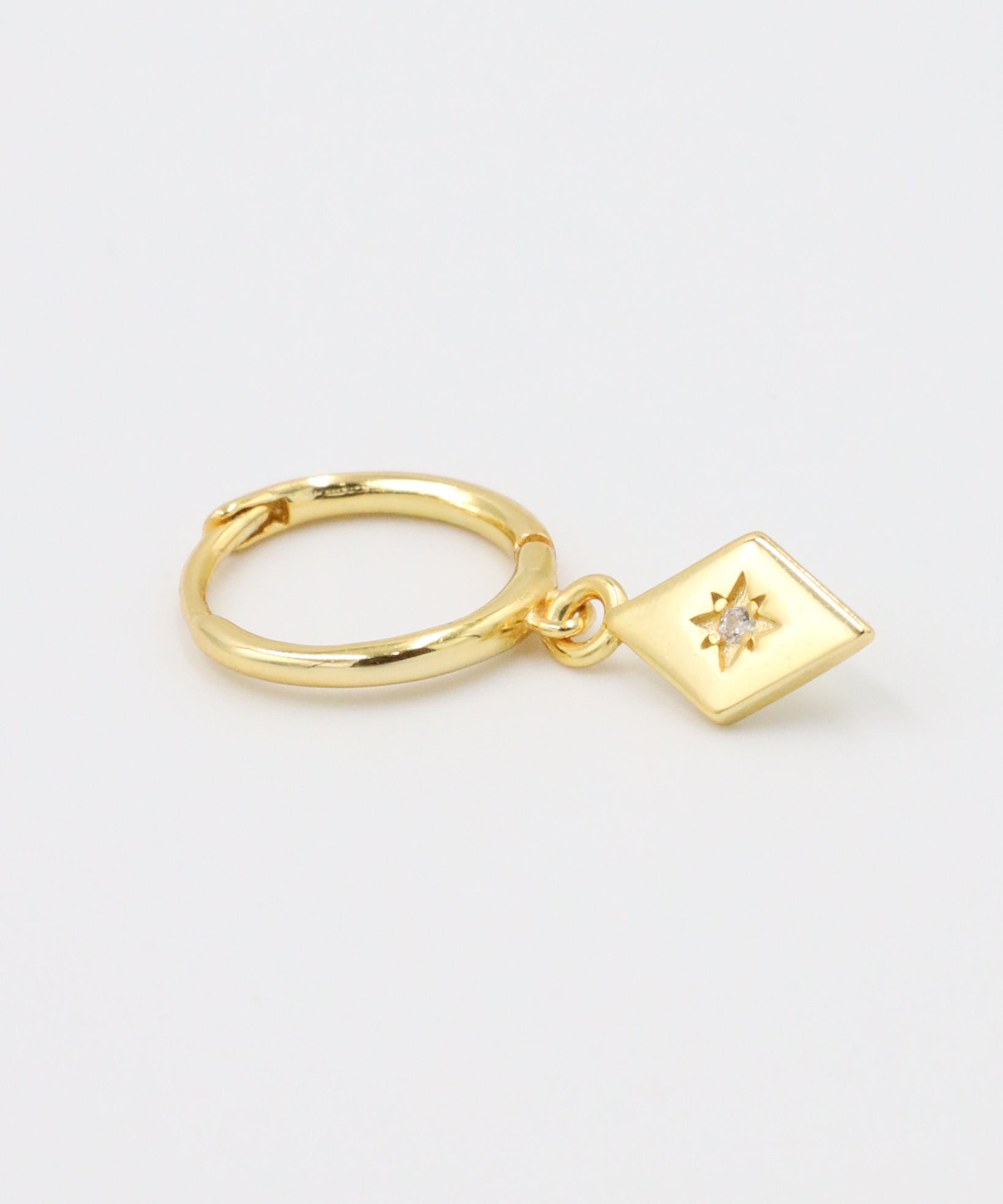 Single Patricia Gold earring featuring a starburst design with a zirconia center, hanging from a gold hoop.
