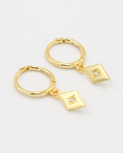 A pair of Patricia Gold earrings featuring a starburst design with a small zirconia in the center, hanging from gold hoops.
