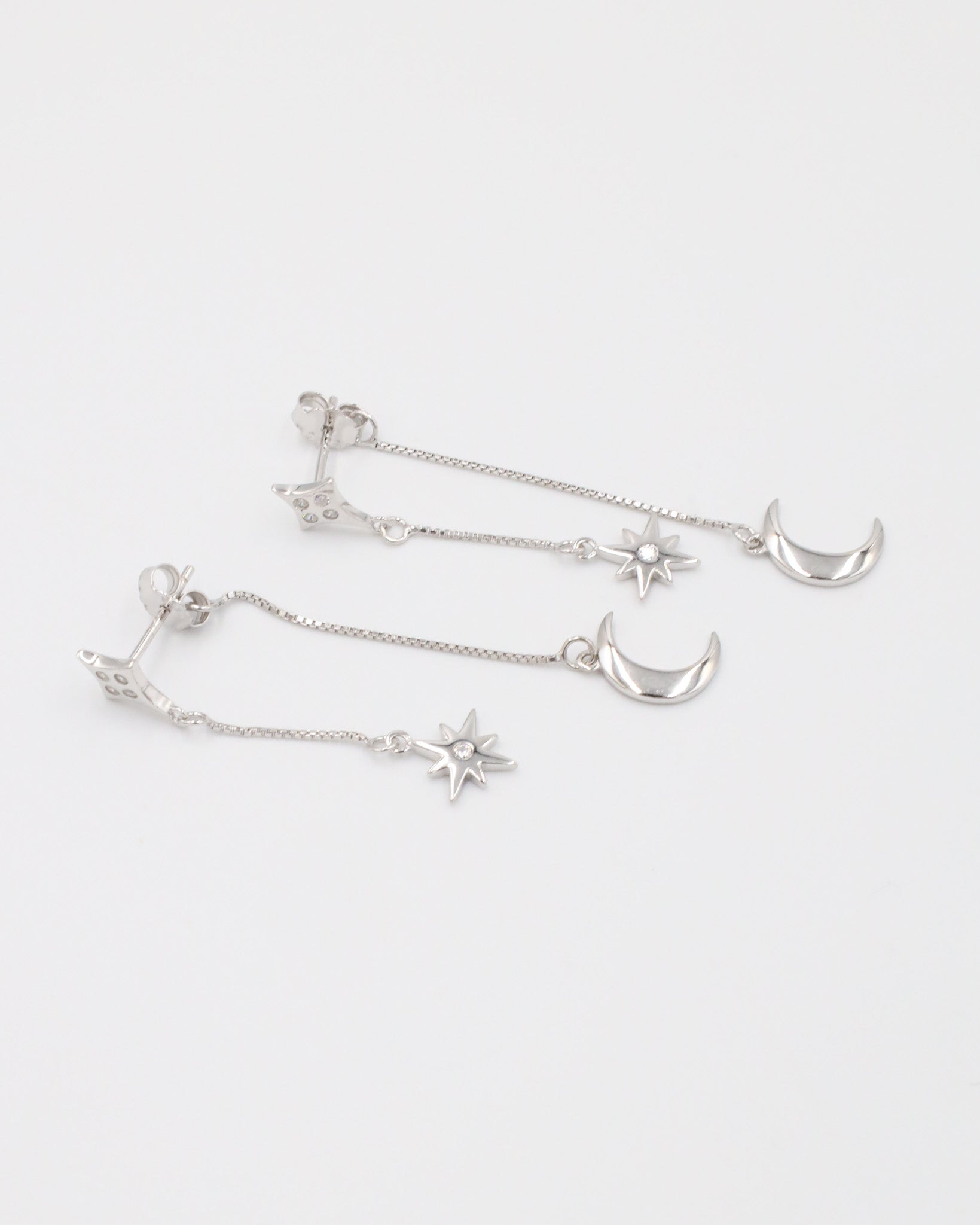 Elegant pair of Reese silver earrings in sterling silver, with moon and star charms on delicate chain drops.