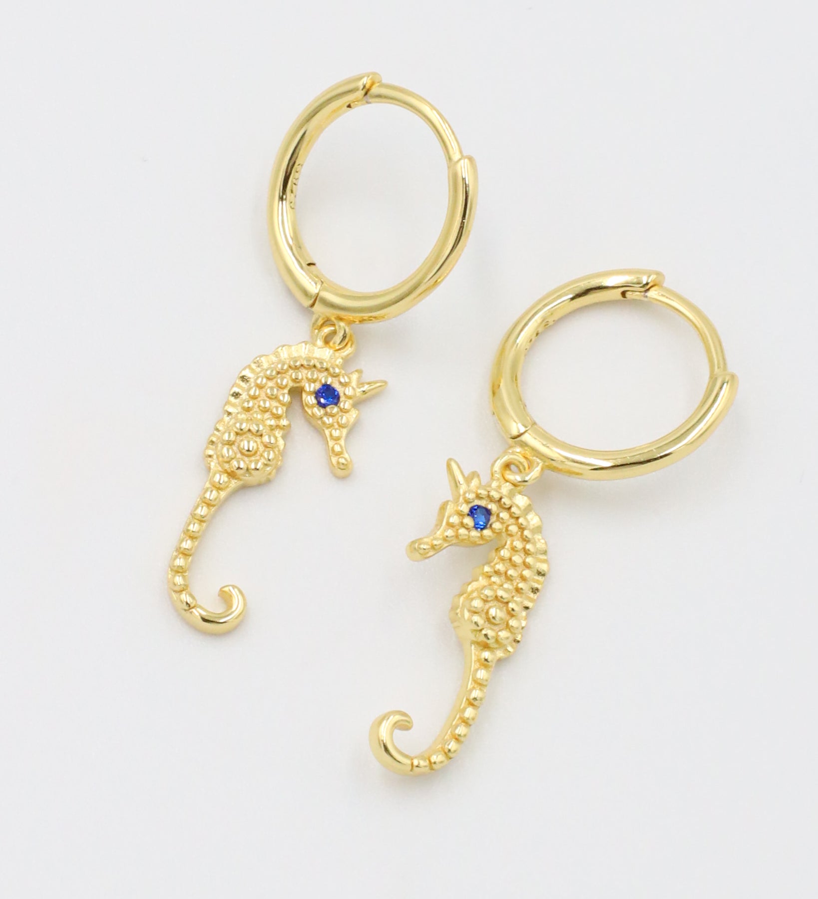 Pair of Seahorse Gold earrings made from gold-plated sterling silver, featuring seahorse charms with blue zirconia eyes.
